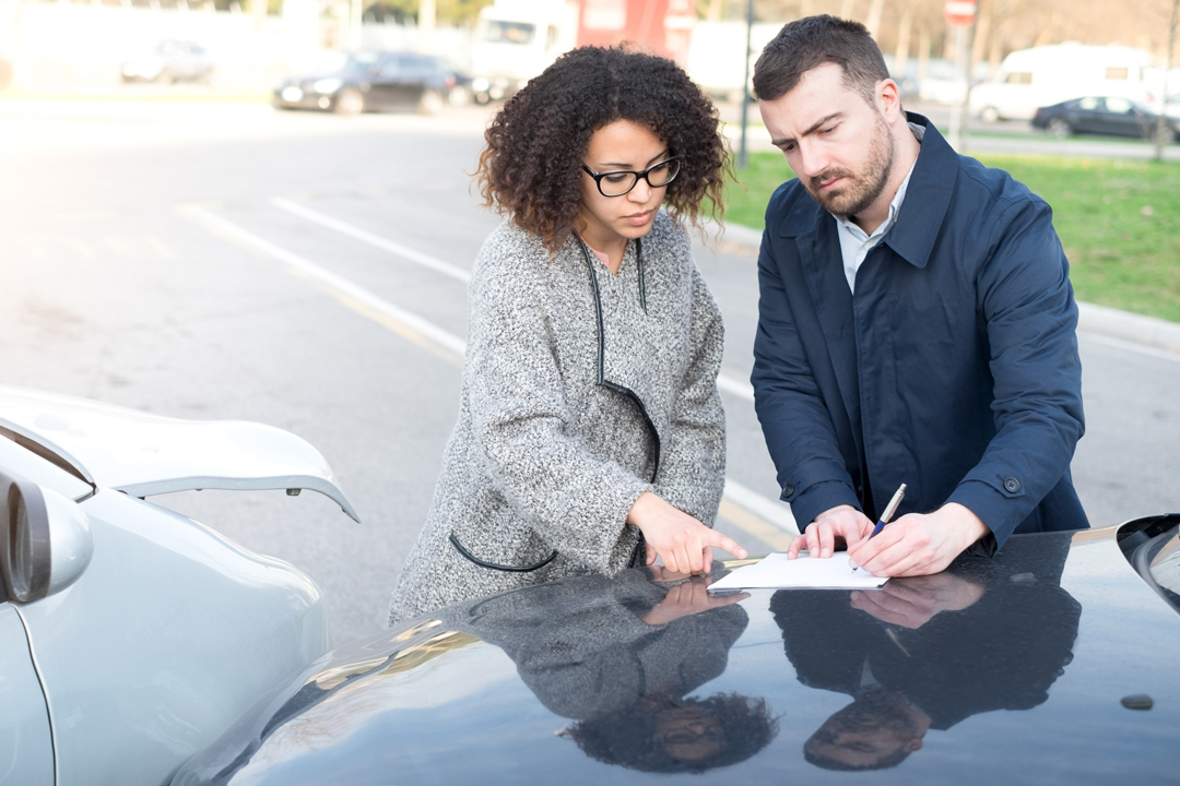 Woman and man filling out insurance forms after a vehicle accident.