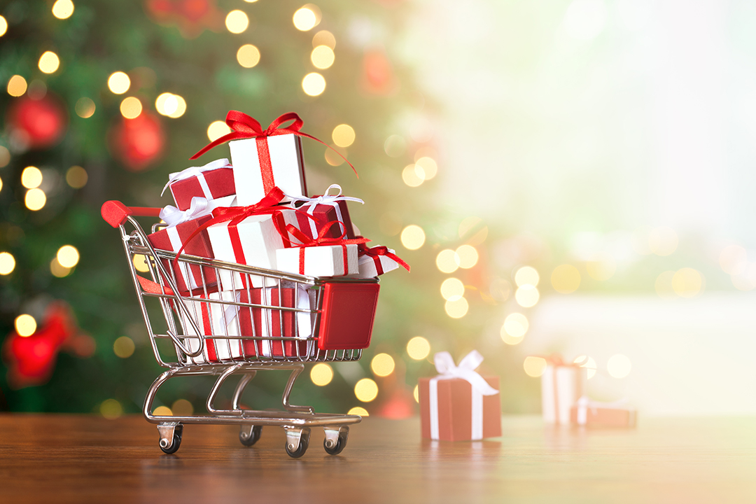 Little shopping cart full of christmas gifts with christmas tree background.