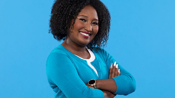 woman employee wearing blue shirt smiling with arms folded and blue background