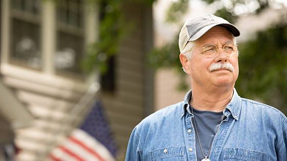 An older man looking out into the distance with an american flag in the back