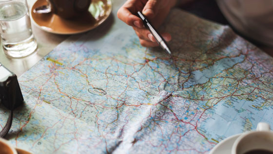 A person holding a pen over a map planning to travel.