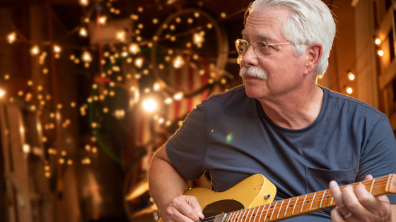 Close up of a grandpa playing his guitar and string lights in the background