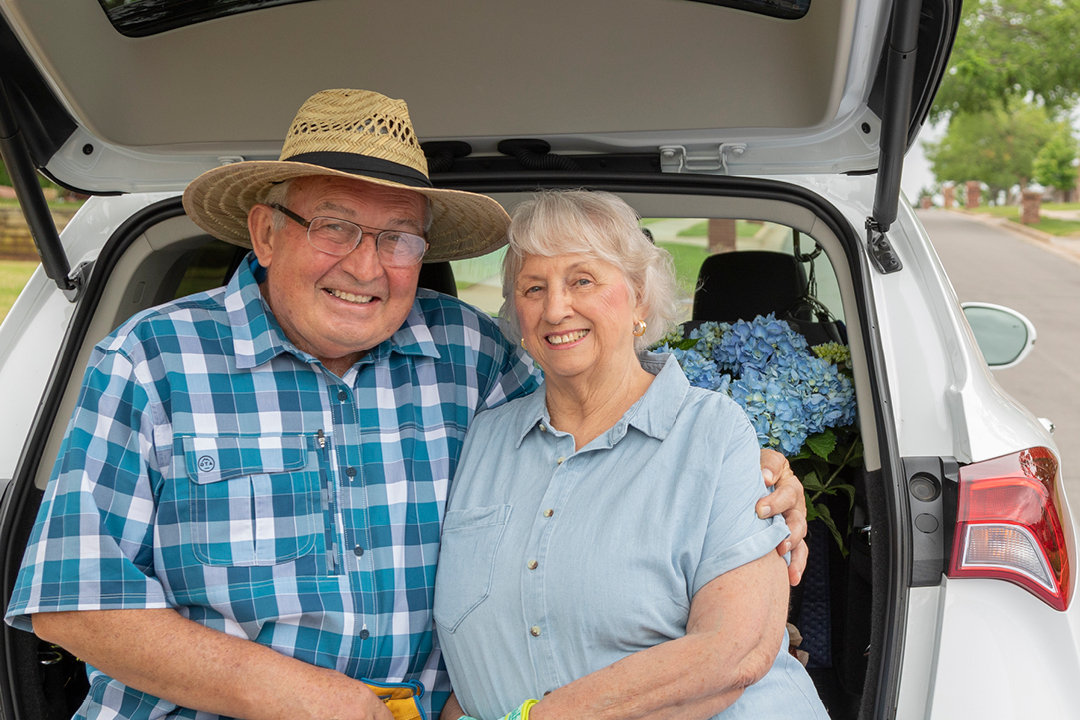 Two older couple sitting in the trunk of a car and hugging