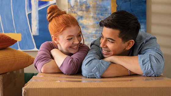 A couple leaning on a box looking at each other.