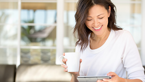 Woman holding mug, looking at her tablet and smiling.