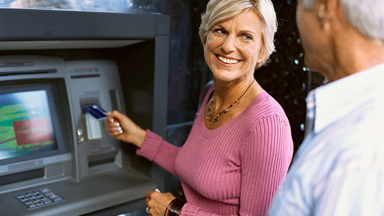 Older woman using ATM while smiling at husband