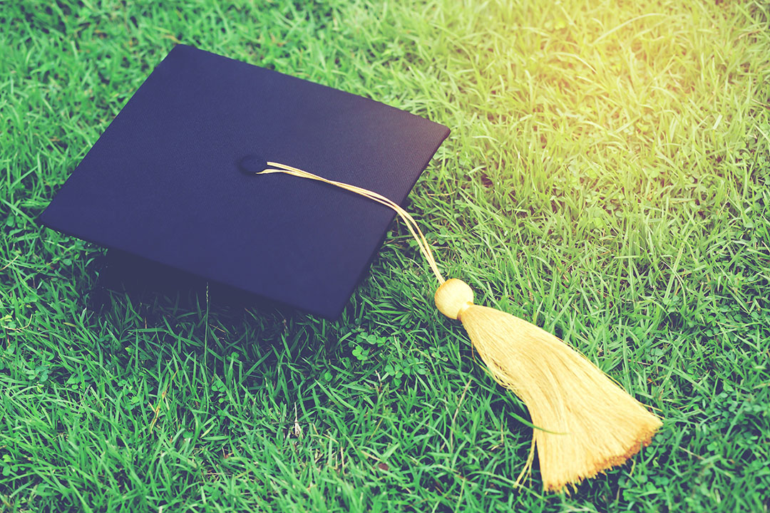 Picture of a navy blue graduation cap with a yellow tassle on the vibrant green grass.